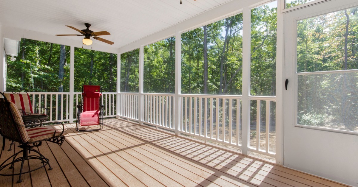 A bright screened porch with striped chairs arranged along wooden floorboards while ceiling fans hang overhead.