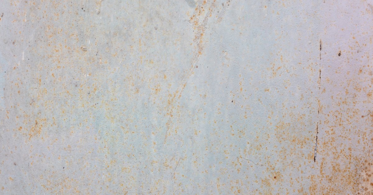 Galvanized Steel Railing Performance Factors A pale metal surface with orange rust spots, scratches, stains, and worn marks spread across the texture.