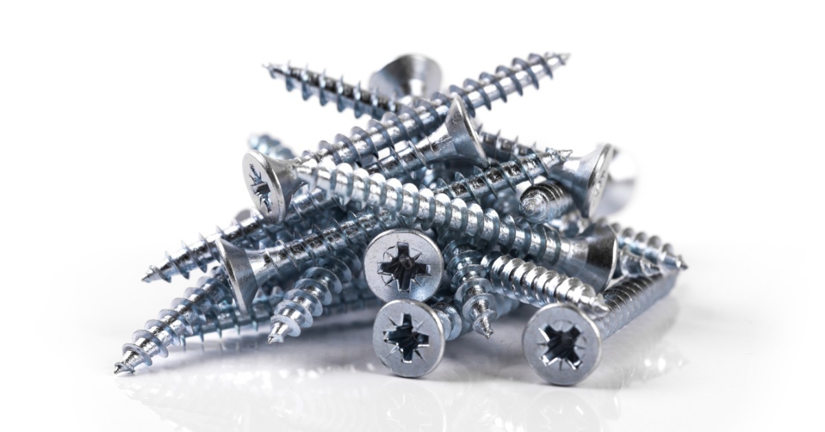 A pile of silver screws with pointed tips and cross-shaped heads resting on a plain white background.