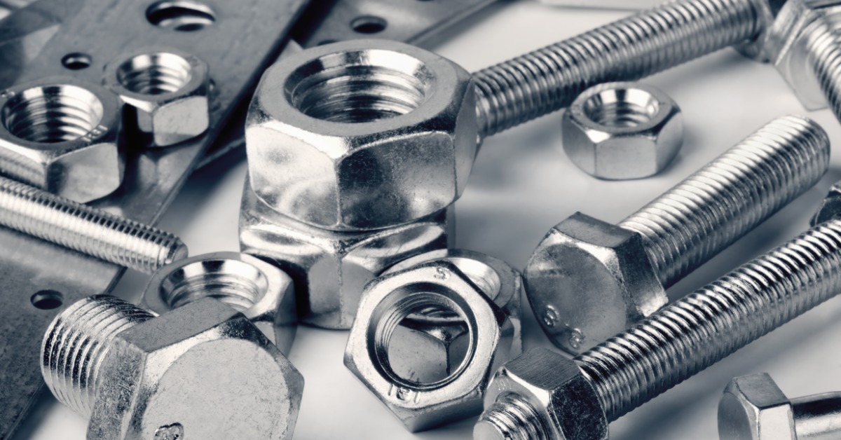 Silver bolts, nuts, and metal plates arranged close together on a plain white surface with shiny finishes.