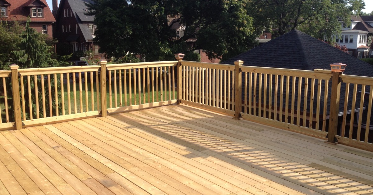 A large wooden deck with nothing on it. The railings are also made of wood. There are some homes in the distance.
