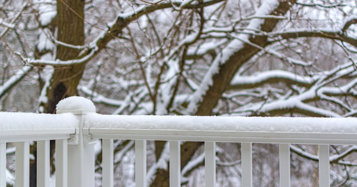 A white deck railing that's covered in a layer of snow. The tree behind it is also covered in snow.