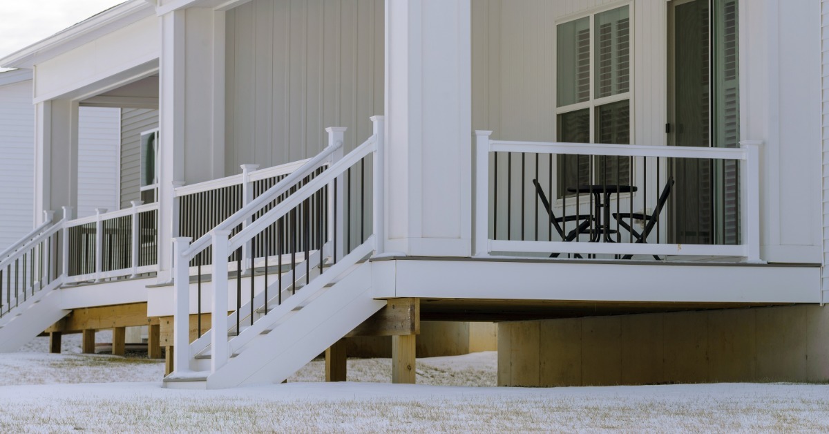 A home with two decks with stairs leading down from them. The ground around them is covered in a thin layer of snow.