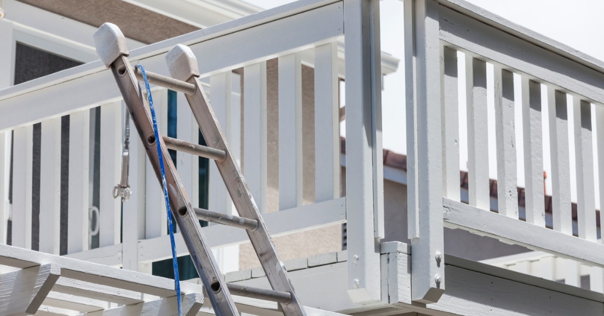 An elevated deck that has a ladder leading up to it. The ladder is leaning against the shade bars of a lower porch.
