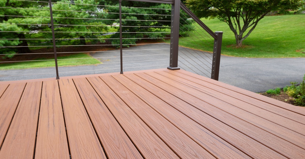 A deck that has a railing with a cable railing leading down the steps. The steps lead to an empty driveway.