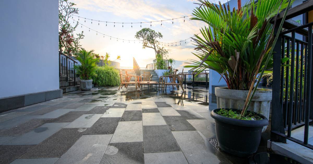 A patio that uses a lot of darker colors throughout its design. There are a bunch of potted plants spread across the space.