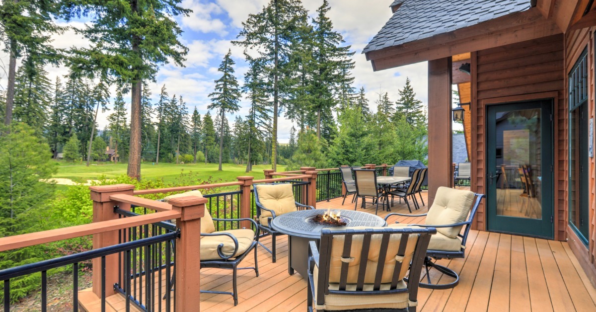 A deck that has two tables, surrounded by chairs. One of the tables has a small fire pit in the center of it.