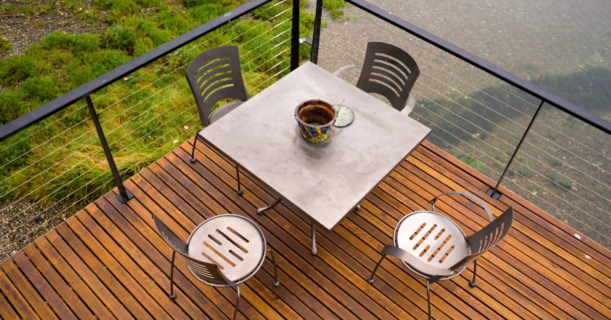 An overhead view of a table and chairs sitting on the corner of a deck. There is a black metal railing around it.