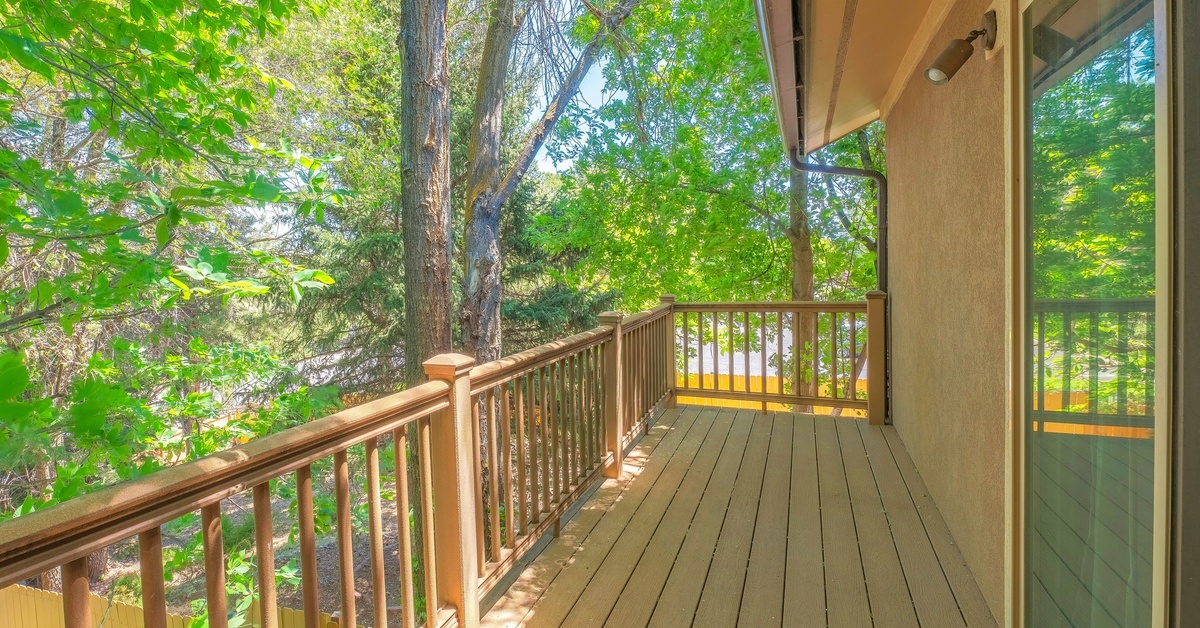 A small deck attached to the second story of a house. The deck is surrounded by a bunch of tall trees.