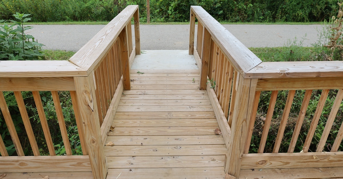 A deck walkway leading down to a sidewalk. There are wooden railings on both sides of this narrow path.