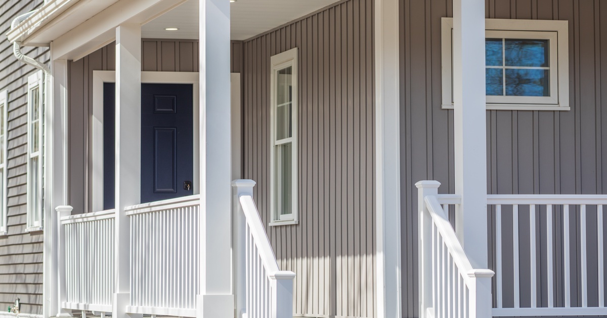 The front porch of a home that has a roof built over it. The railings lead to a set of stairs that head towards the ground.