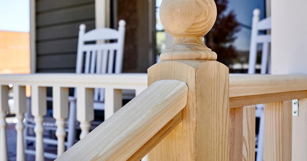 A close-up view of the wooden post of a deck. The post has a ball topper, and there are some rocking chairs behind it.