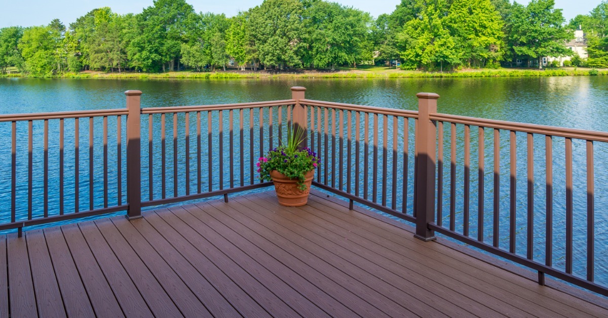 A wooden deck with a vinyl railing overlooking a small lake. There are a bunch of trees on the other side.