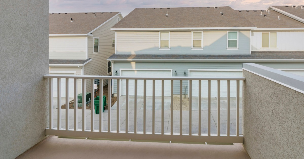 A small deck with railing overlooking neighborhood garages and houses beneath puffy sunset clouds in the distance.