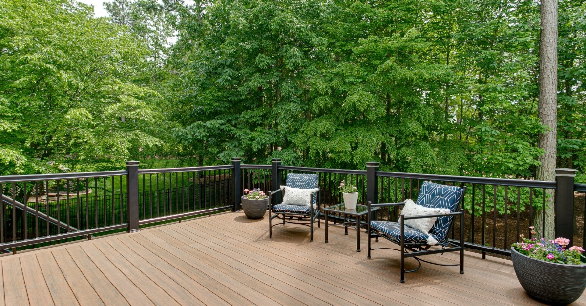 A staged summer deck with outdoor seating, flower pots, and surrounding woods creating a natural setting.
