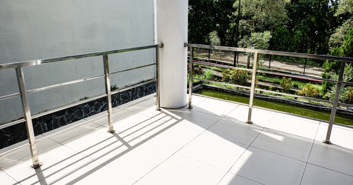 A tiled balcony with steel railings overlooking a green garden and pond. There is a walking path further in the background.