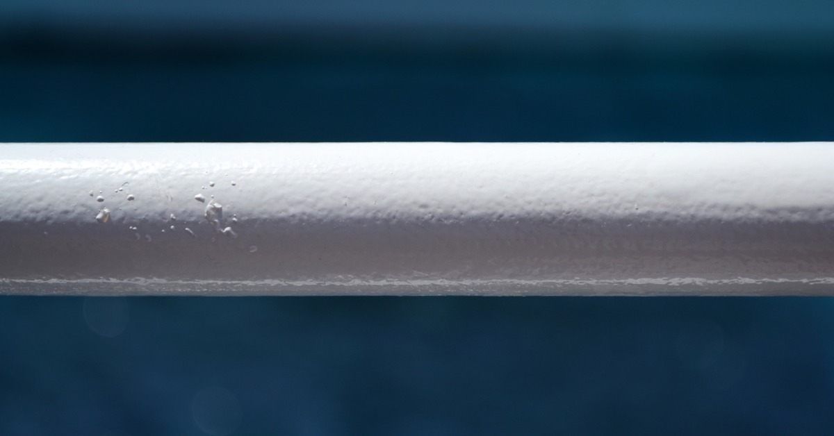 A close-up of a section of white metal railing running horizontally with water in the background behind it.