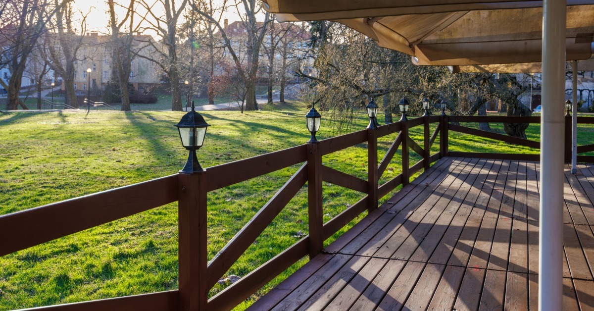 A wooden terrace with railings, lantern posts, and an overhead awning. There is a grassy yard in front of the deck.