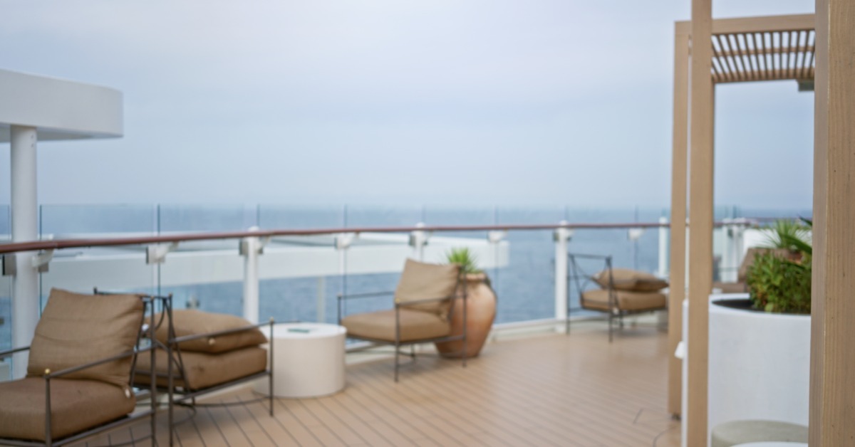 A deck with chairs and tables set up next to a glass railing, looking out over an ocean horizon, creating a soft backdrop.