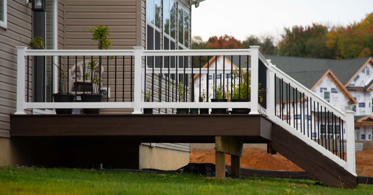 A raised deck with white railing posts and black balusters extending from a house beside a grassy yard.
