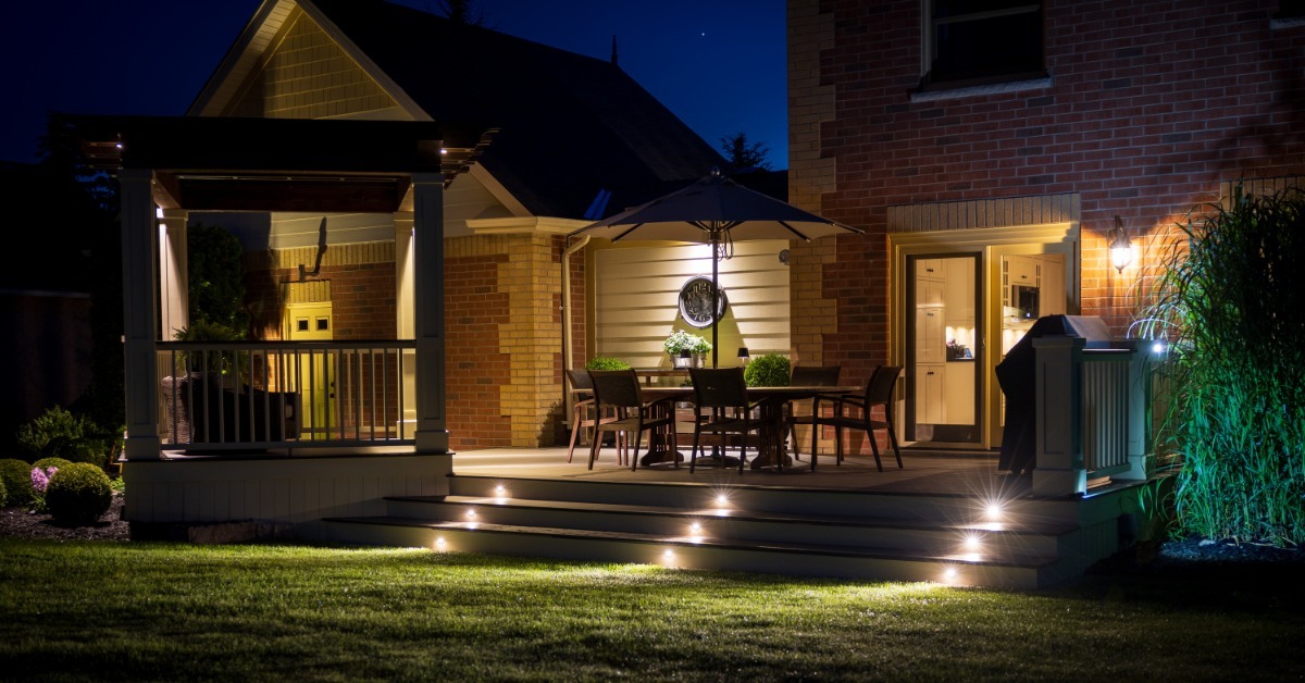 A custom deck and pergola glowing at night beside a house, with steps that have lights built into them.