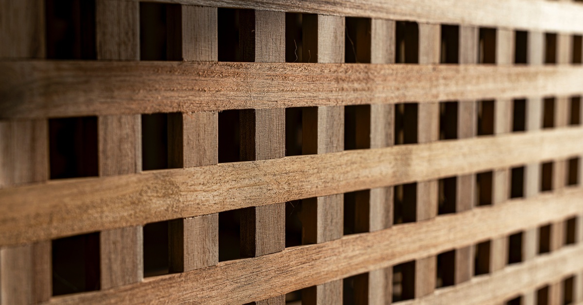 A close-up of a wooden lattice panel with rectangular slats crossing over natural grain in warm brown tones.